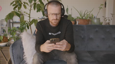 medium close front angle of a man sitting on a couch scrolling and swiping and typing on an iphone