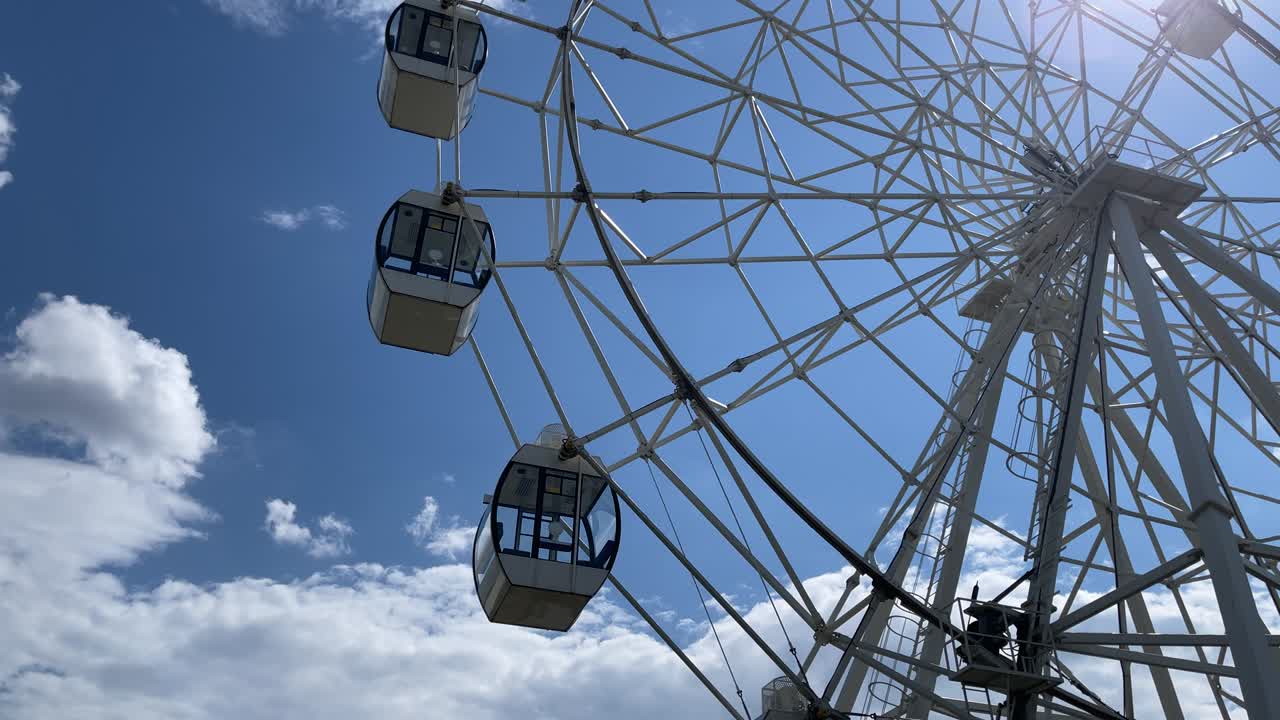 Close up of rotating ferris wheel on background of cloudy sky. Entertainment attraction with overview of city in summertime