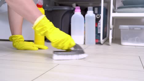 the human hands in yellow protective glove pour out the soap cleanser from plastic bottle and clean the ceramic floor, making circular motions with brush. housekeeping, housewife daily routine concept