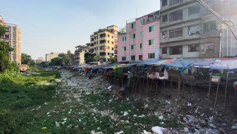 environment pollution, trash pile in dry canal beside slum in a city - panning slow motion shot