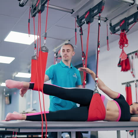 personal trainer is helping his female client at the modern rehabilitation center. young woman is lying on a special table on one side and doing exercises with suspension ropes.