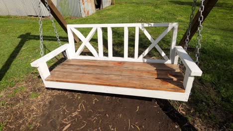 Large-empty-wooden-porch-chair-swings-in-the-breeze-in-backyard-on-sunny-day