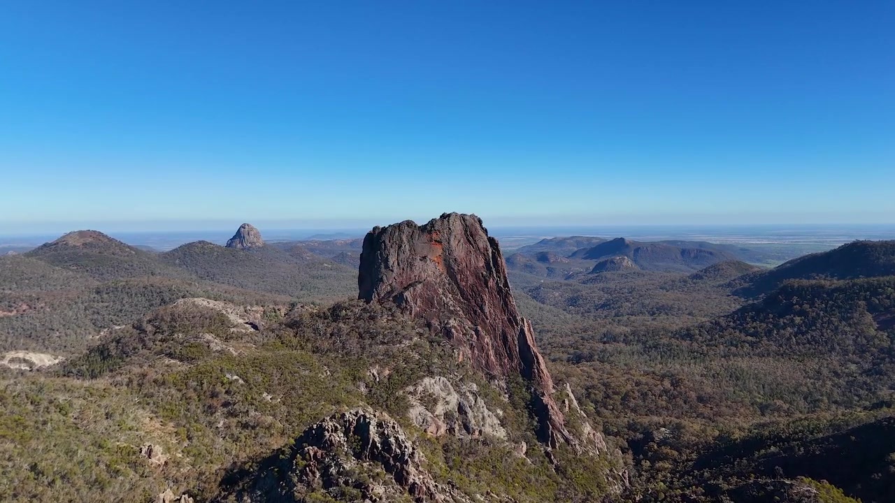 Vidt luftfoto av vulkanske fjellformasjoner under klar blå himmel i Warrumbungle nasjonalpark.