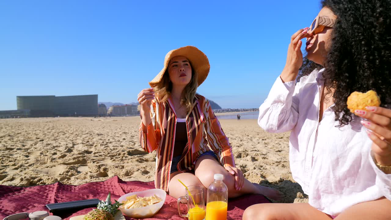 To unge kvinner nyter en piknik på en solfylt strand