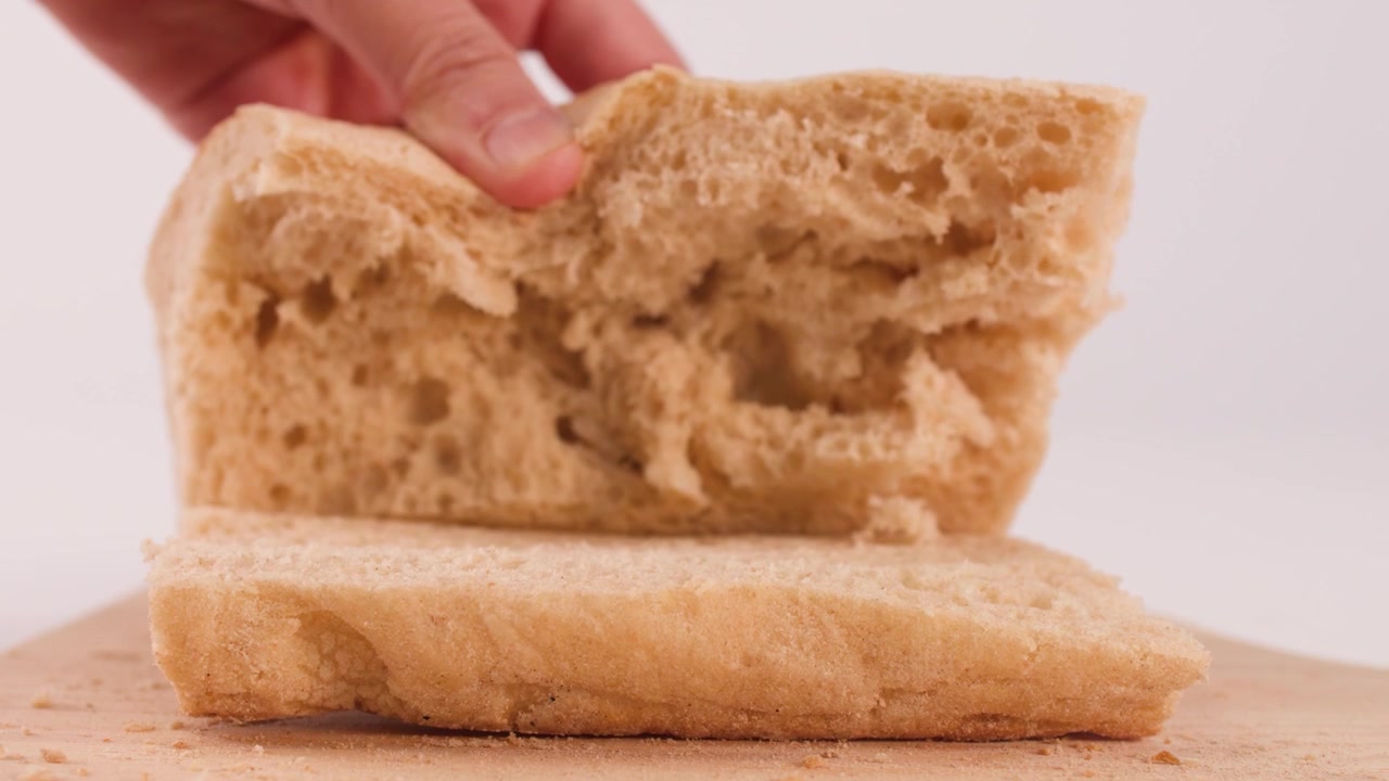 Close-up shot of hands opening a sliced loaf of fresh bread on a wooden surface.