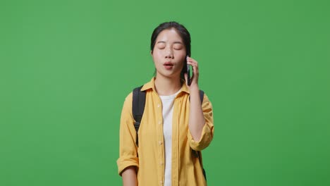 asian woman student with a backpack talking on smartphone while standing in the green screen background studio