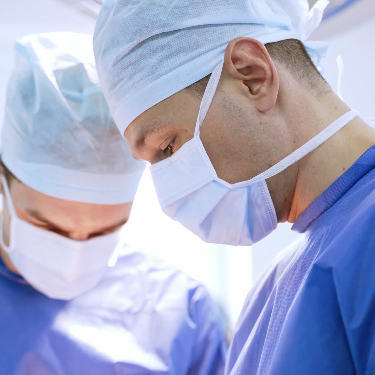Faces of surgeons in masks in a hospital operating theatre. Doctors wearing medical protective uniform performing a surgery. Healthcare concept.