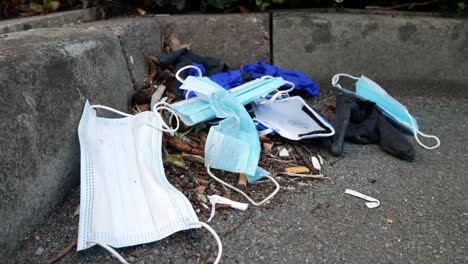 dirty filthy disposable corona virus face masks and latex gloves among cigarette rubbish on street curb rising dolly left