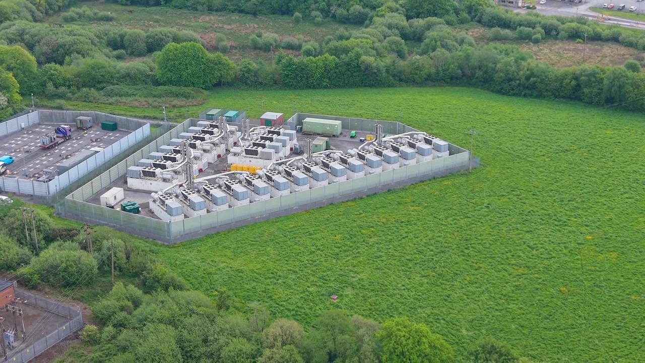 Descending Drone View of Modern Gas Peaking Plant with exhaust stacks, generators, cooling systems. Facility provides rapid-response electricity to the grid during peak demand. BESS in Construction UK