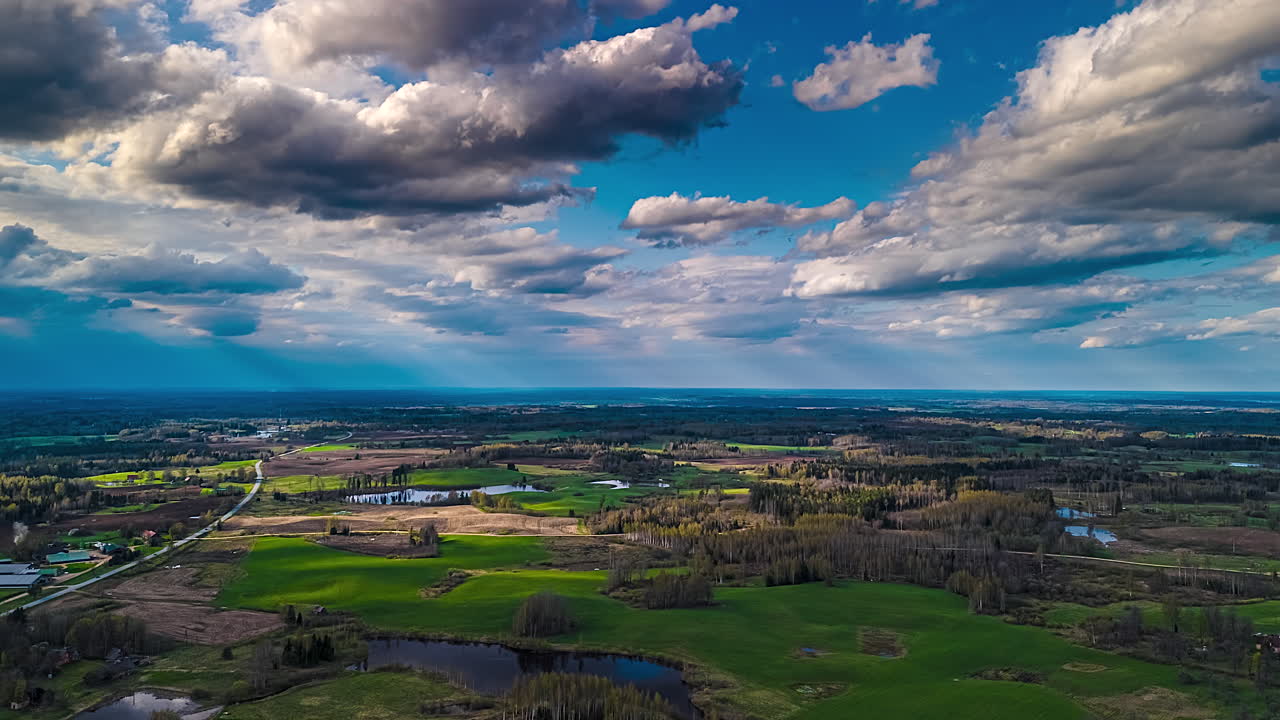 Timelapse of shifting clouds over patchy green farmland and forest lines