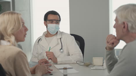 a young black doctor in a facemask listening to a ederly couple 1