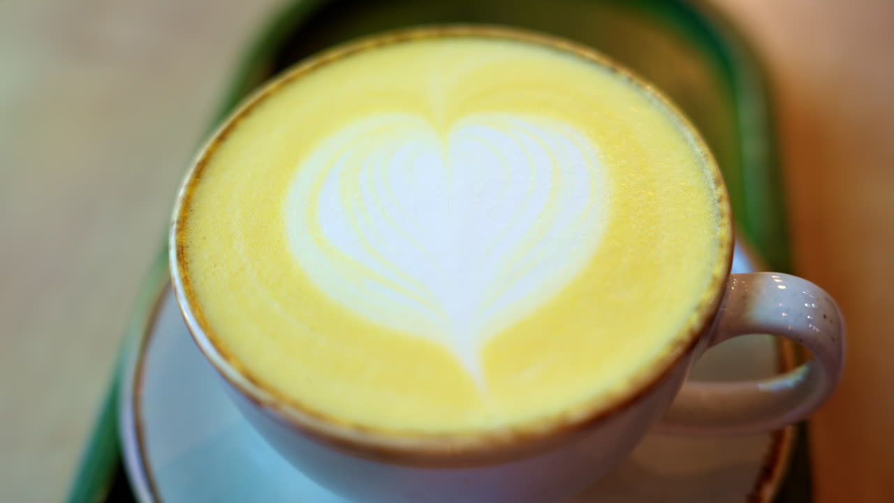 Close up of a cup of yellow turmeric latte with a heart design