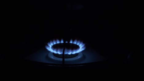 gas burner on, glowing with blue flame, at night in kitchen. close-up
