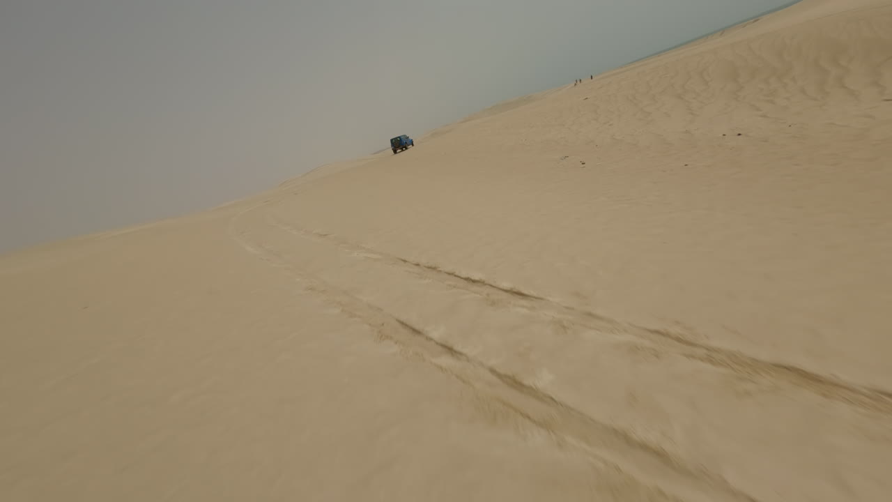 SUV drives up sandy hill in desert landscape under clear skies in Oman