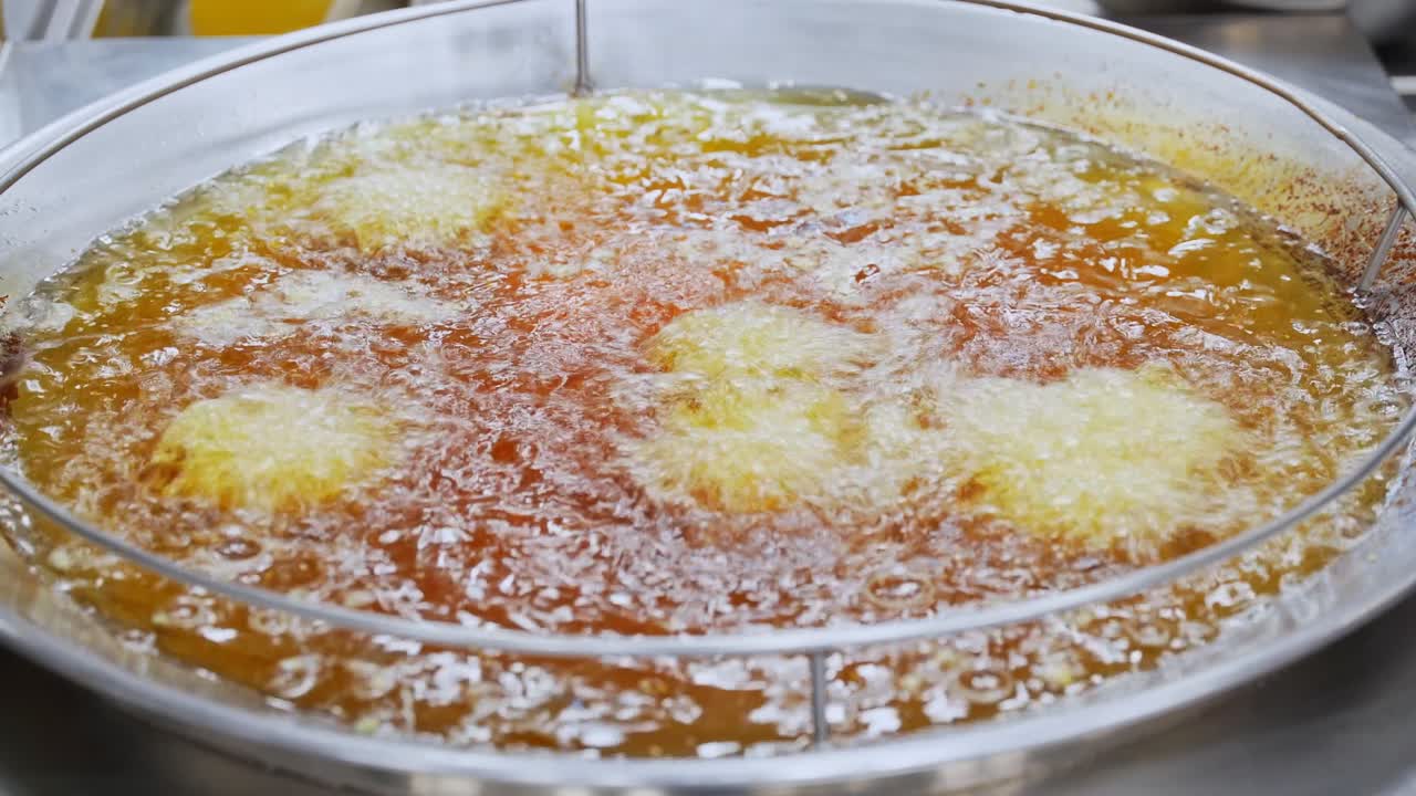 Close-up of gloved hand deep frying food in hot oil at a commercial kitchen. Perfect for food prep, industry, or fast-food visuals