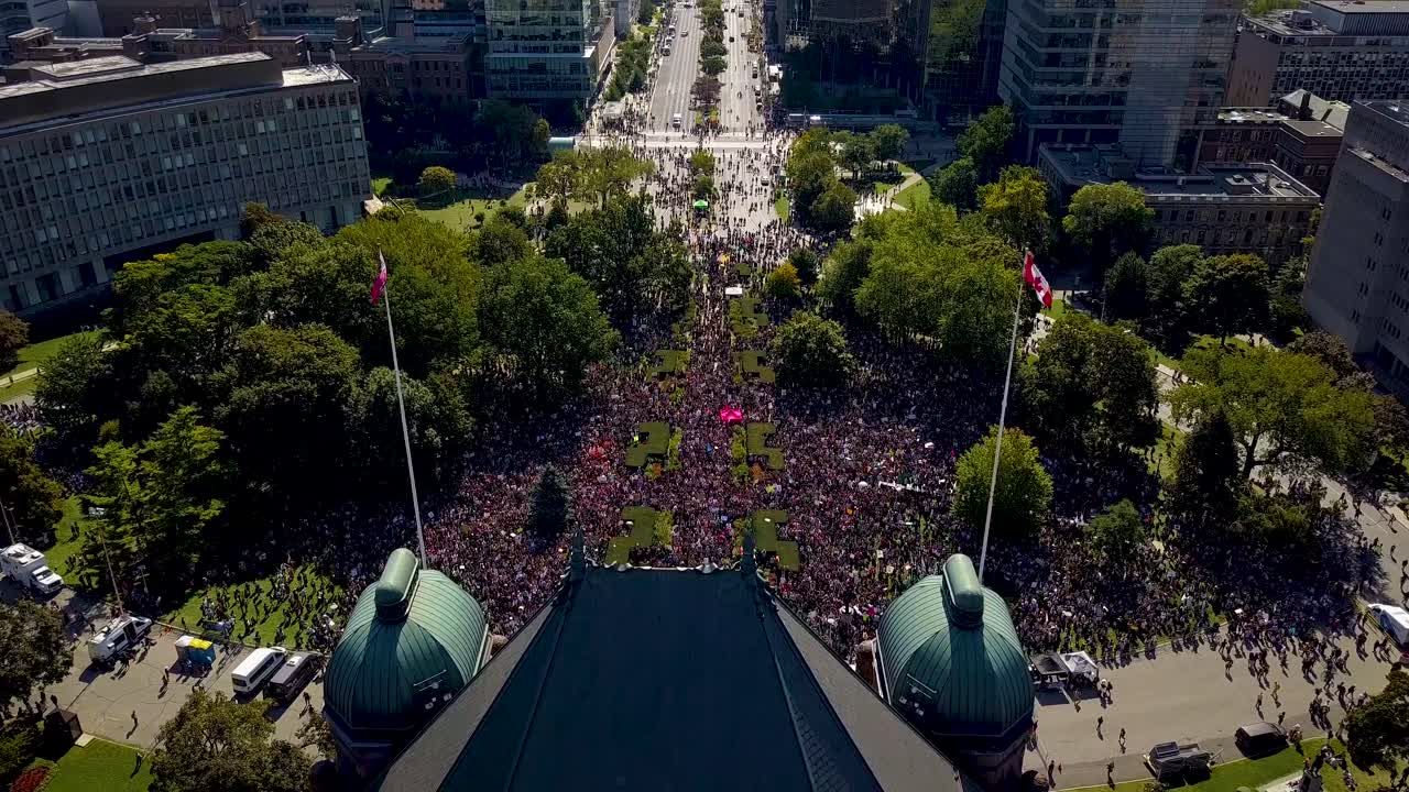Aerial Reveal of big crowd gathered at government building in Toronto. Drone shot over Ontario Legislature in downtown, tilt down to people protesting for Climate Change Action. Wide outdoor day in 4k