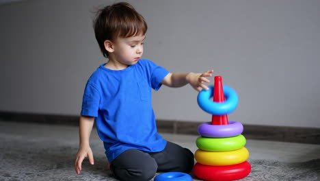 smiling caucasian boy plays with a toy pyramid. kid puts the rings on the basis cheerfully and then starts again.