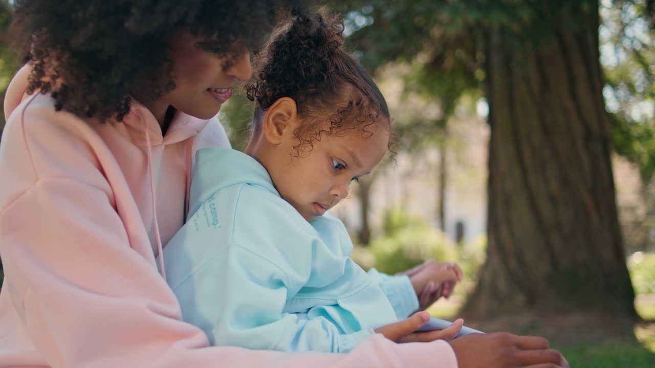 Woman daughter watching cartoon on smartphone sitting green meadow close up.