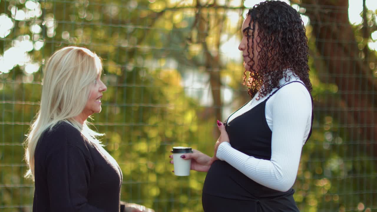Two women, one pregnant, having a friendly conversation outdoors