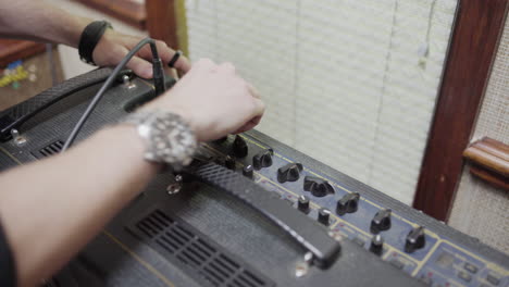 man plugs in guitar amp and adjusts knobs, inside, close up, handheld
