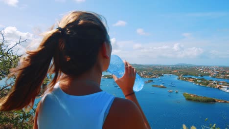 girl hiker drinking water bottle while admiring a harbor in curacao, caribbean