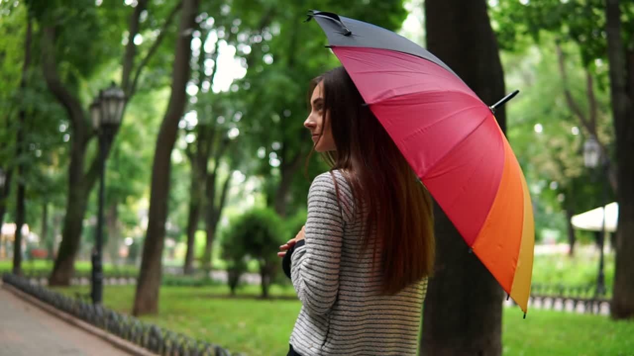 vista de atrás y mujer atractiva girando su colorido paraguas en un día de lluvia en el parque de la ciudad