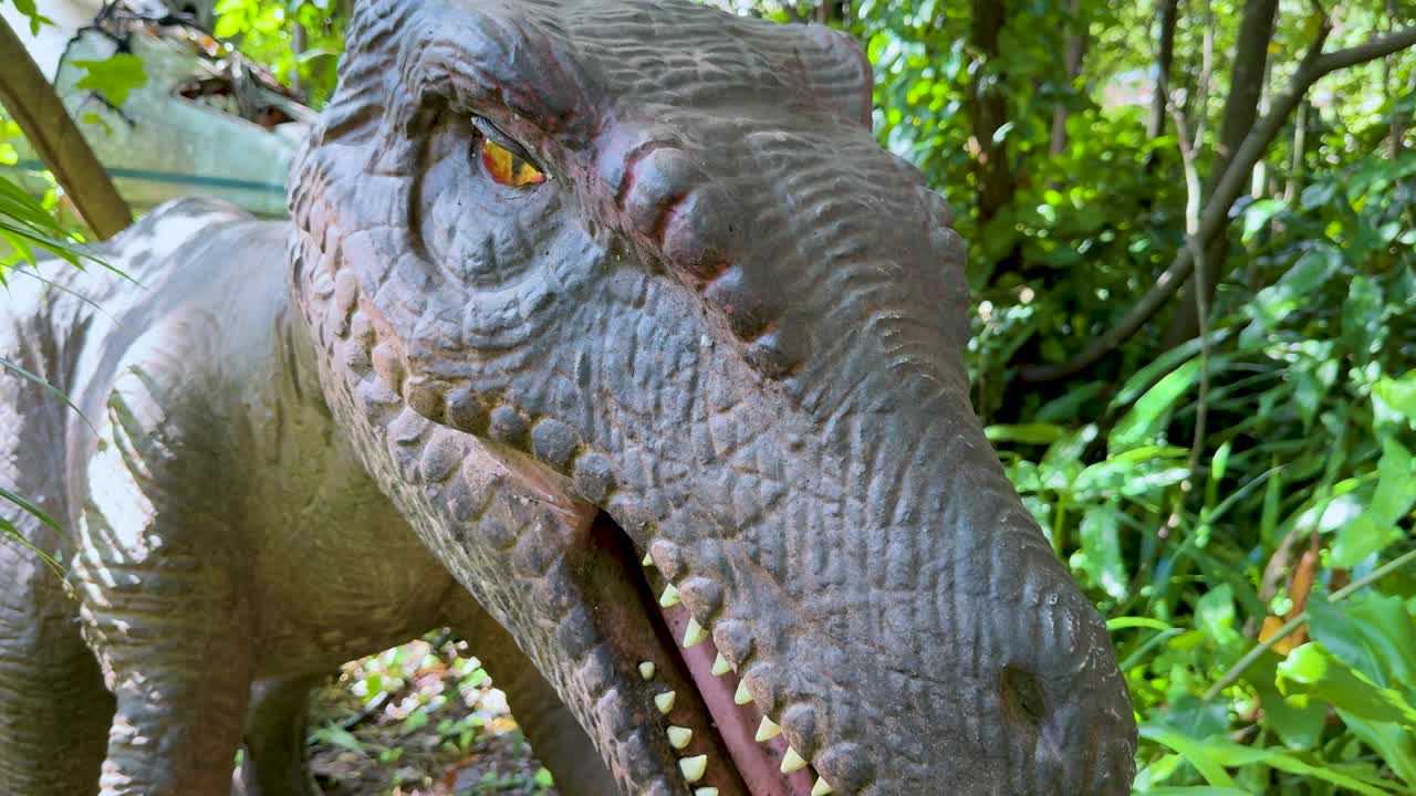 Realistic animatronic dinosaur head moves and blinks in bright, natural outdoor park lighting