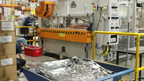 worker placing sheet metal in bin, power press operating in background