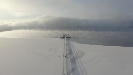 Drone-shot-of-Bridge-to-a-small-island-on-a-frozen-lake-in-Dalarna,-Sweden