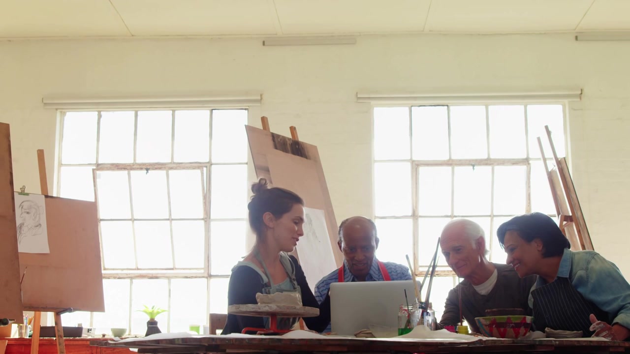 Mentor de pie gesticulando hacia un portátil, grupo trabajando en un estudio de arte con una superposición azul que muestra ideas.