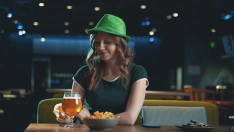 bella giovane donna che beve birra e indossa un cappello verde irlandese