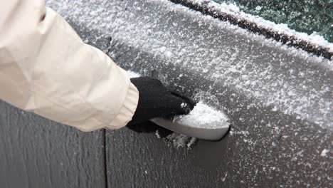 hand in black glove trying to open frozen car door handle during winter