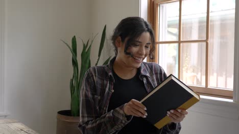 Complacida-Mujer-Puertorriqueña-Mirando-A-La-Cámara-Sonriendo-En-Adoración-De-Su-Nuevo-Libro-De-Lectura