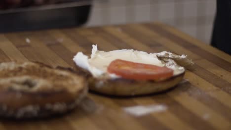 primer plano extendiendo queso crema y agregando tomates en bagel