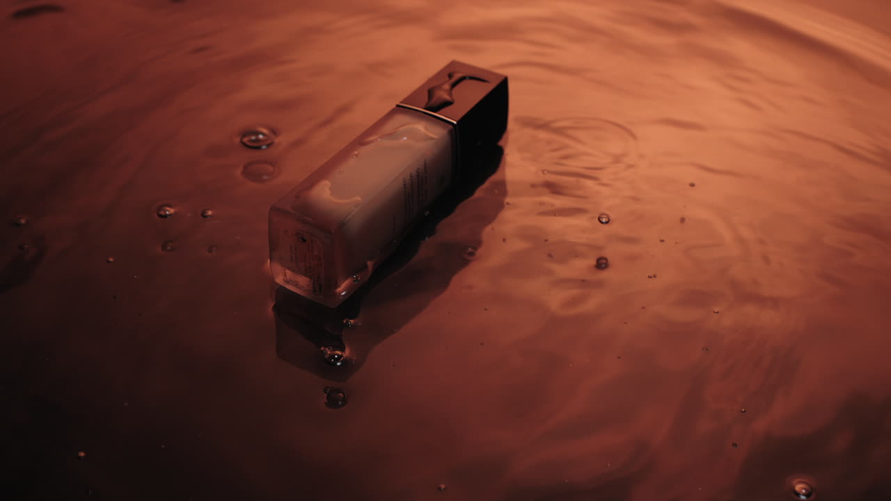 la caída de una botella de perfume cosmético en un agua poco profunda se refleja creando una onda de agua