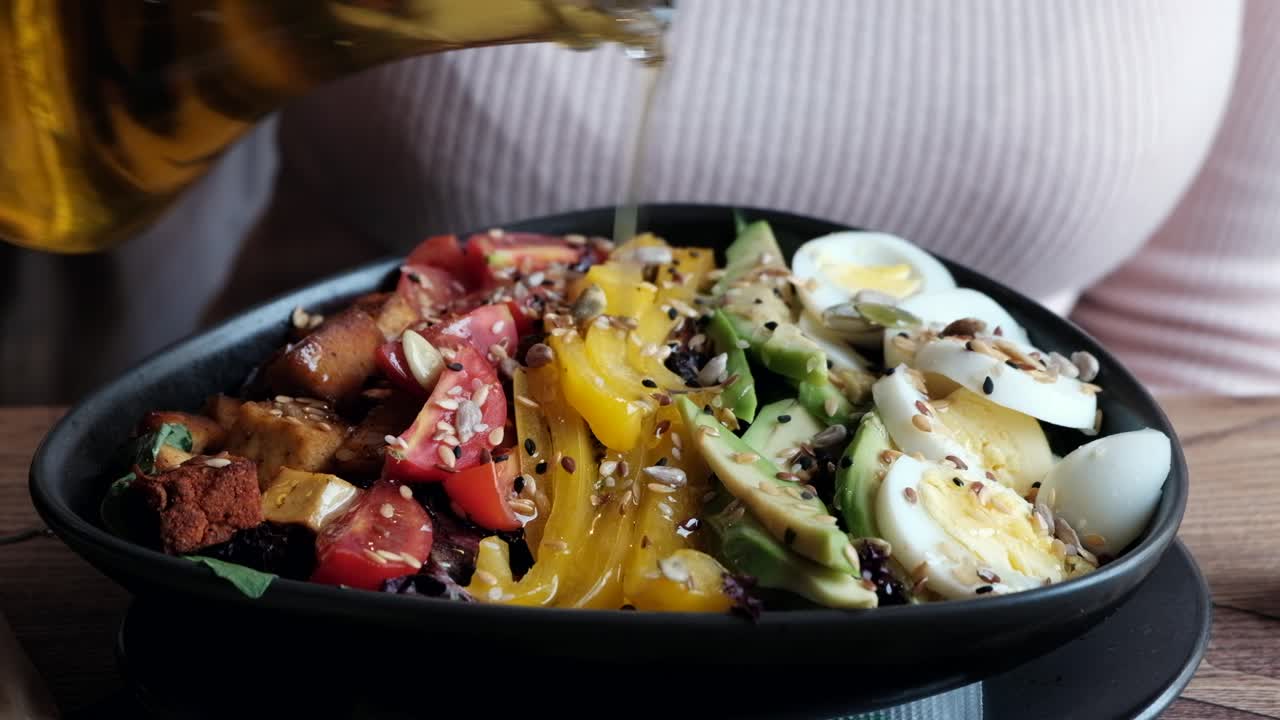 Woman pouring oil on a salad in a black bowl at a restaurant
