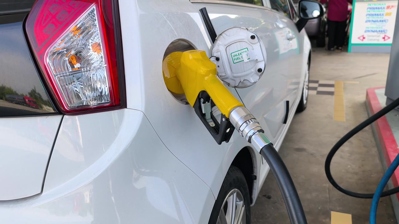 A fuel nozzle is inserted into a car gas tank to pump petrol. The vehicle gets refueled at a service station during a road trip.