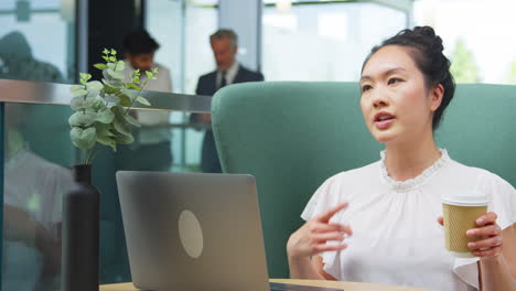 businesswoman having video call on laptop at table in breakout seating area of office building