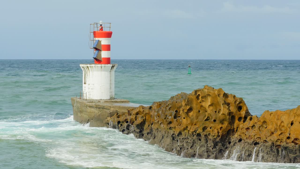 Slow motion view of waves crashing against basalt rock next to port-side marker at harbor entrance at Pasaia bay