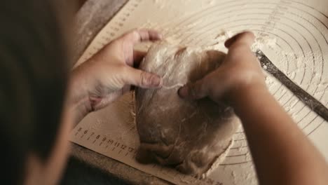 young boy coats gingerbread dough in flour on table, over shoulder