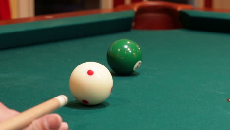 closeup of person playing pool shooting solid green 6 ball into corner pocket after practice strokes using cue ball with red spots, open bridge hand with wooden cue stick and green felt or cloth