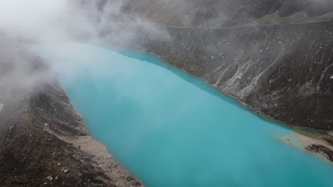 Ascending-drone-shot-of-a-turquoise-lake-inthe-highlands-of-Peru-surrounded-by-clouds