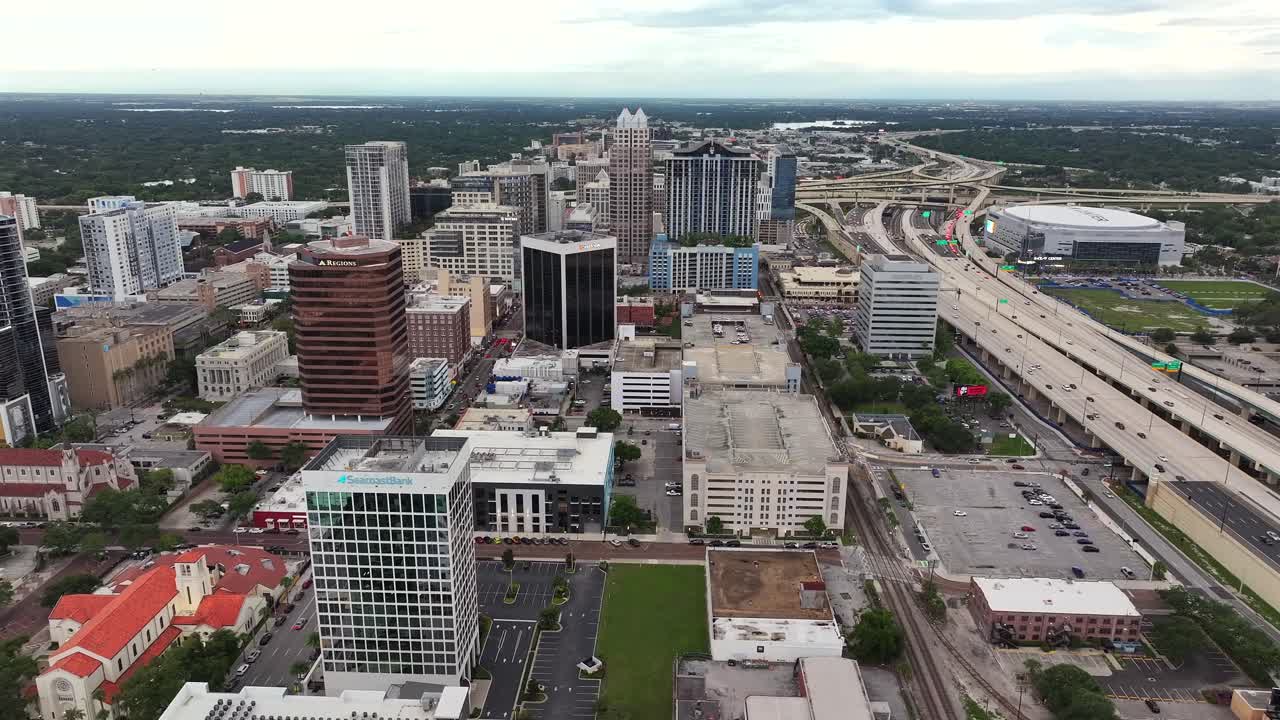 Downtown of Orlando with skyscrapers buildings and busy I-4 Express highway in Florida. Daytime with clouds and green landscape in background. Aerial orbit wide shot.