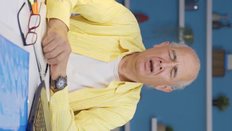 Vertical-video-of-Home-office-worker-old-man-yawns-and-relaxes-at-the-camera.