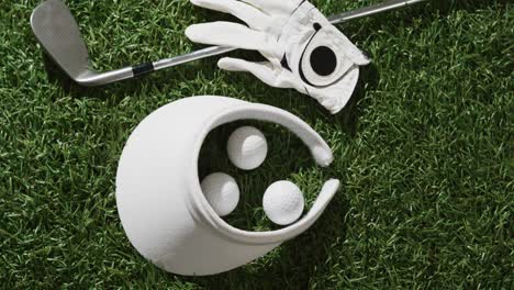 close up of golf club, balls, glove and peaked cap on grass, copy space, slow motion