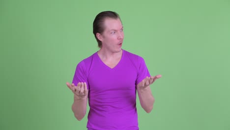 studio shot of young man looking shocked and surprised in disbelief against green background