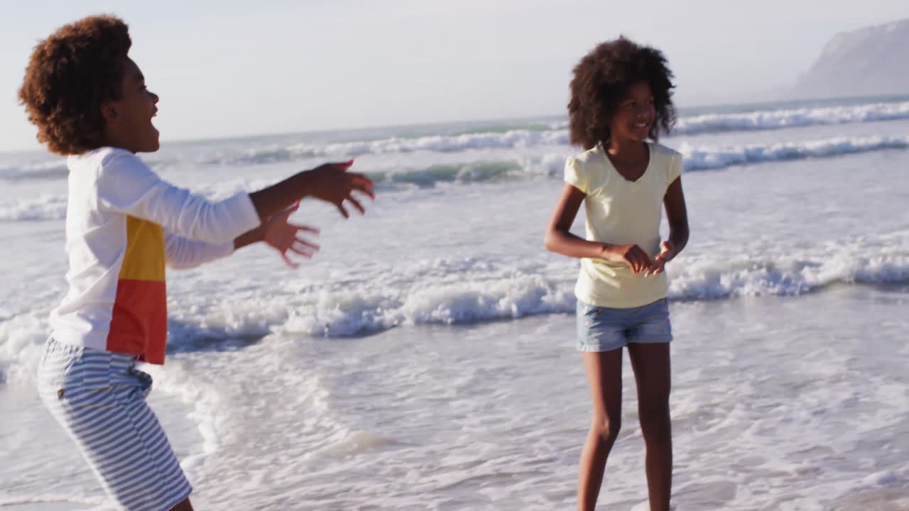 Afroamerikanische Mutter und ihre Kinder spielen Ball am Strand.