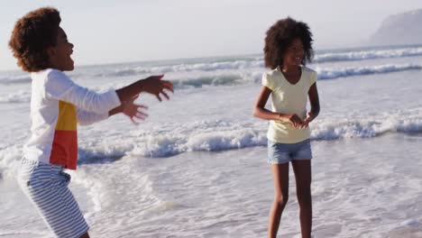 madre afroamericana y sus hijos jugando con una pelota en la playa