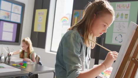 video de una estudiante caucásica concentrada de pie en un caballete pintando en la clase de arte, espacio de copia