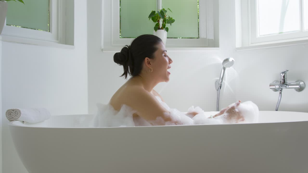 Adult female lifting, blowing foam, shaping and checking foam, moving toward hand shower in bathtub